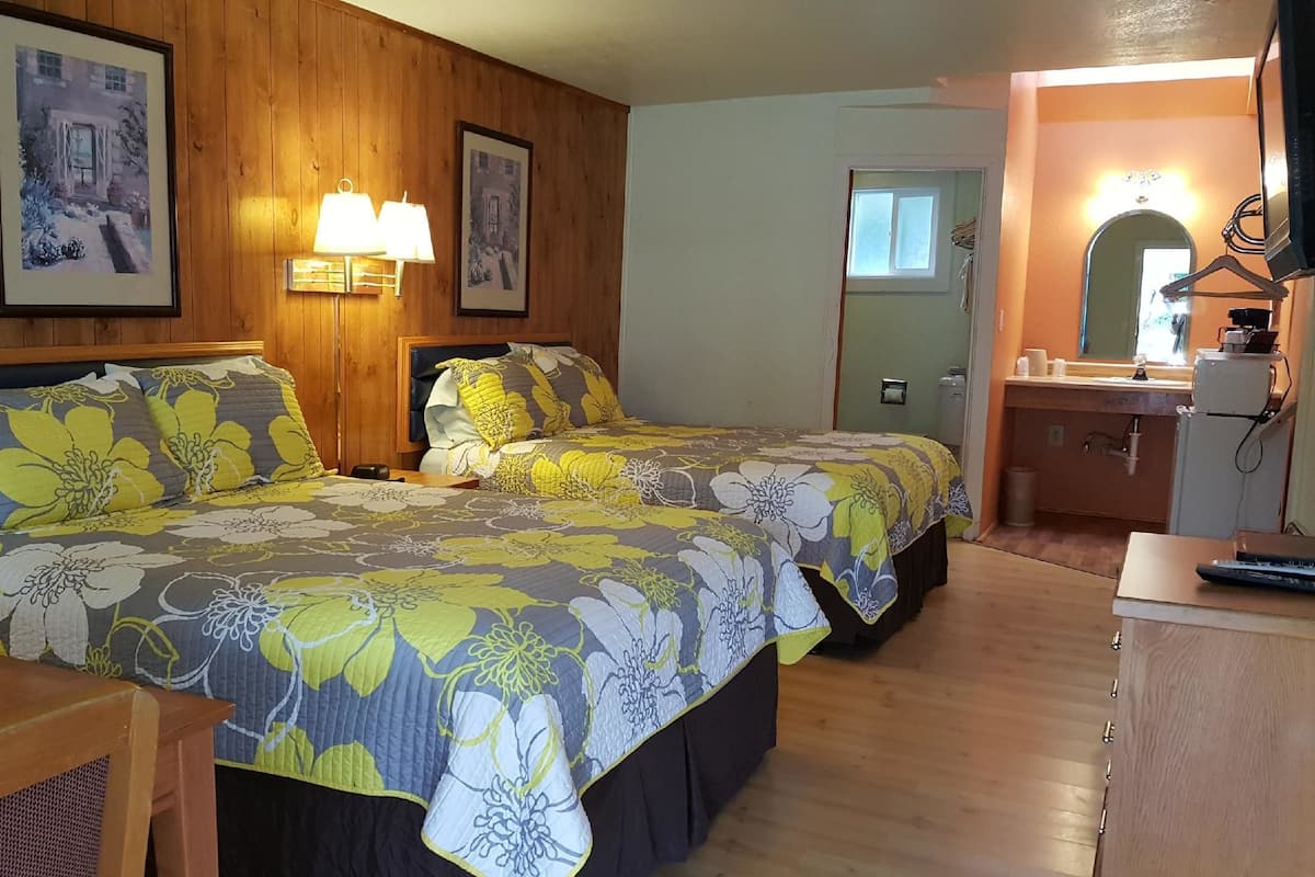 Une chambre avec deux lits, des murs en bois, un bureau et un miroir.