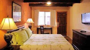 A hotel room with a bed, two bedside lamps, a desk with a chair, a television, and a wardrobe.
