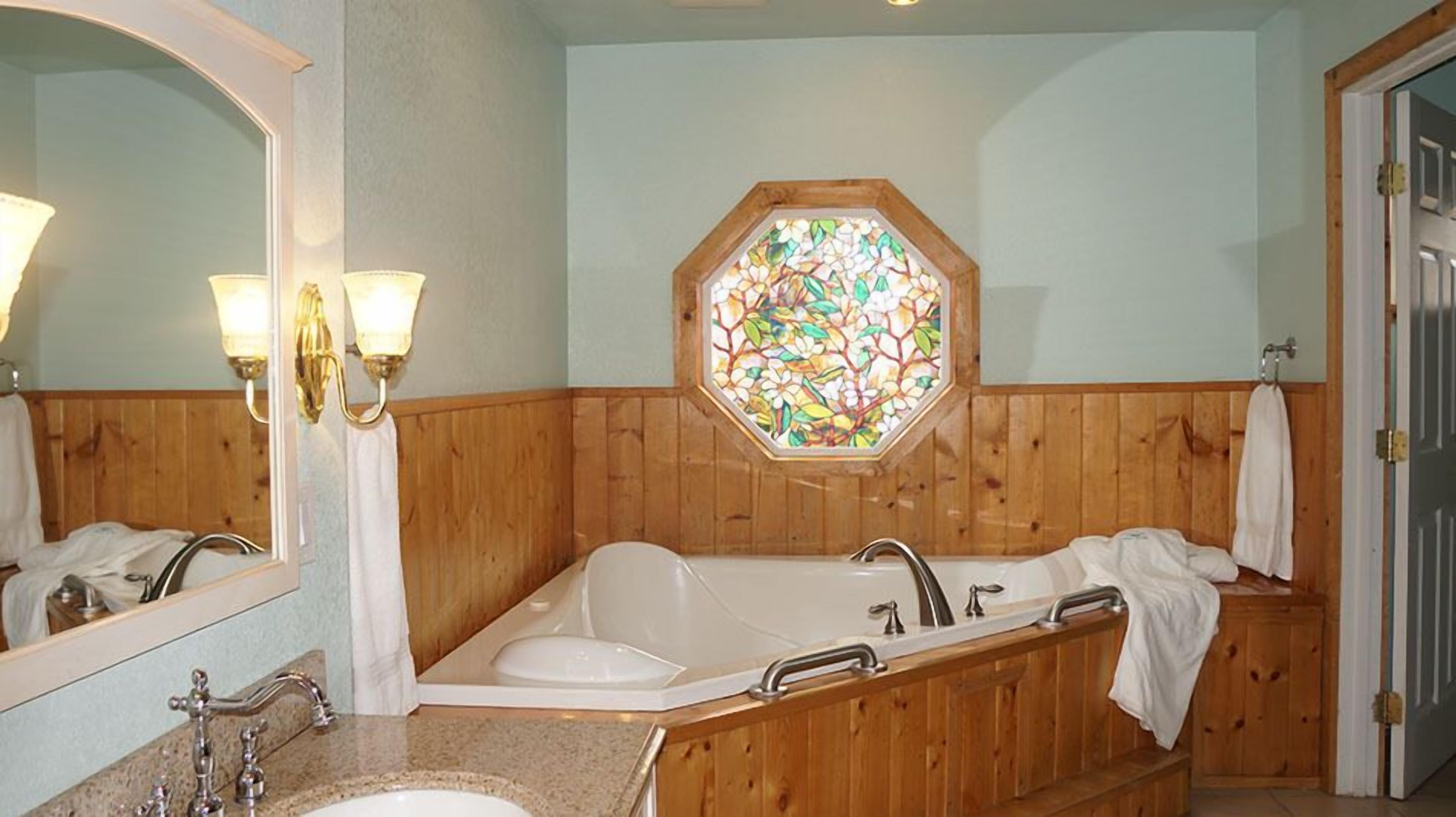Casa de banho com painel de madeira, um espelho grande, uma pia dupla, uma banheira e um vitral.