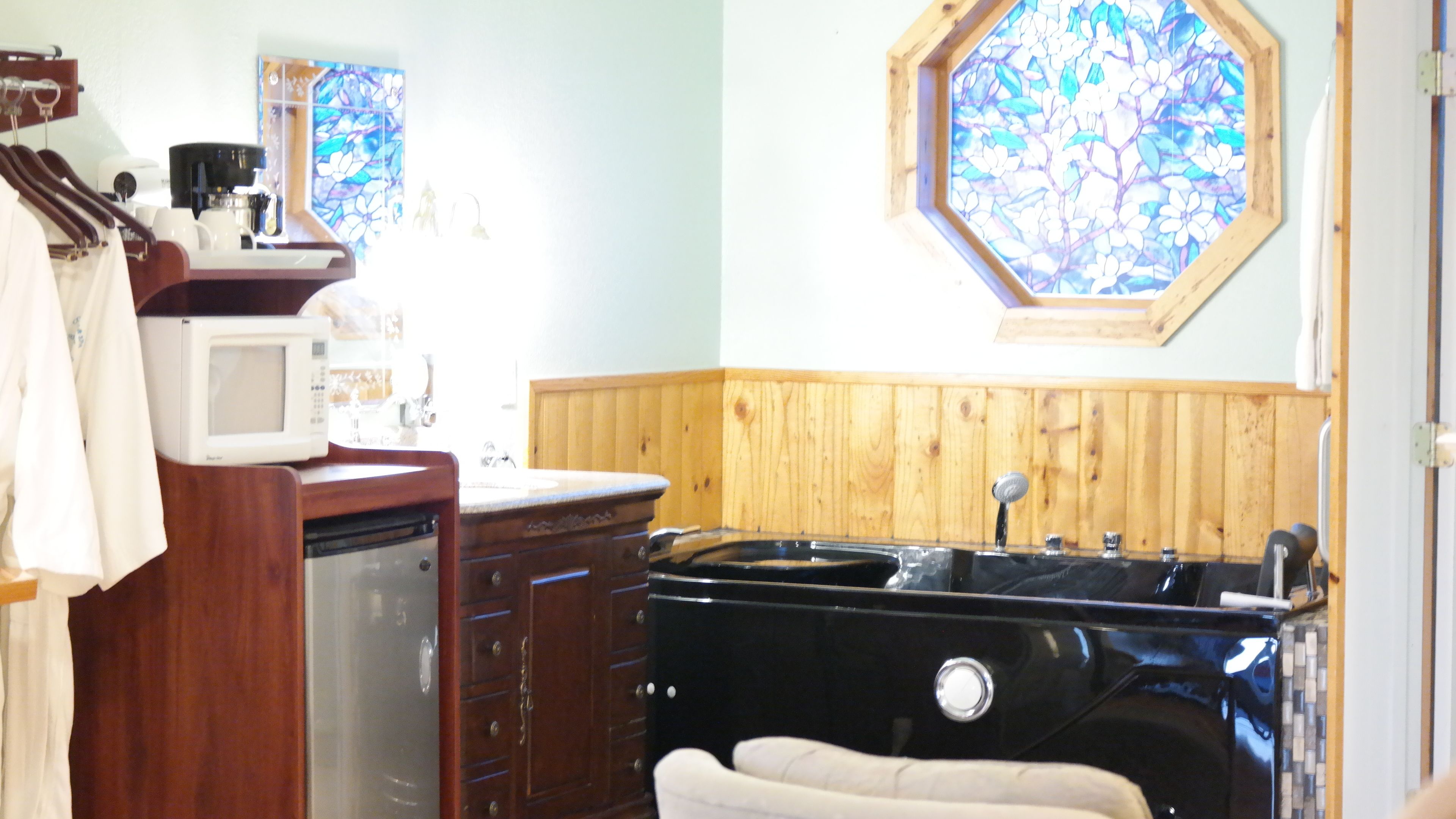 A bathroom with a wooden vanity, a black bathtub, a white sink, and a stained glass window above the bathtub.