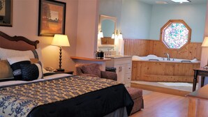 A bedroom with a large bed, a nightstand, a lamp, a dresser, and a bathroom with a bathtub and sink. - Coast Inn and Spa Fort Bragg (Fort Bragg)