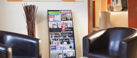 Zona de recepción con dos sillones de cuero, una mesa con una revista y un tablón de anuncios con diversas publicaciones.