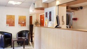 Zona de recepción con mostrador de madera, dos sillones de cuero negro, una pequeña mesa y carteles en la pared.
