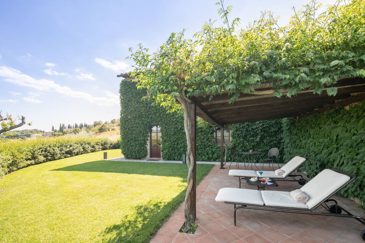 Un patio con dos sillones de descanso, una pérgola cubierta de enredaderas y un seto bien recortado.