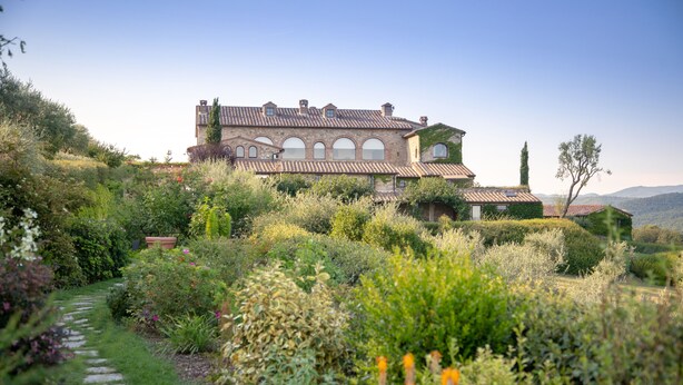 A large, historic building with a tiled roof and multiple windows, surrounded by lush gardens and a stone pathway. - Hotel Le Fontanelle (Castelnuovo Berardenga)