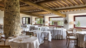 A restaurant with stone pillars, wooden beams, and white tablecloths. Tables are arranged for dining. - Hotel Le Fontanelle (Castelnuovo Berardenga)