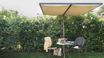 An outdoor patio with a table and two chairs, a yellow umbrella, and a basket of flowers.