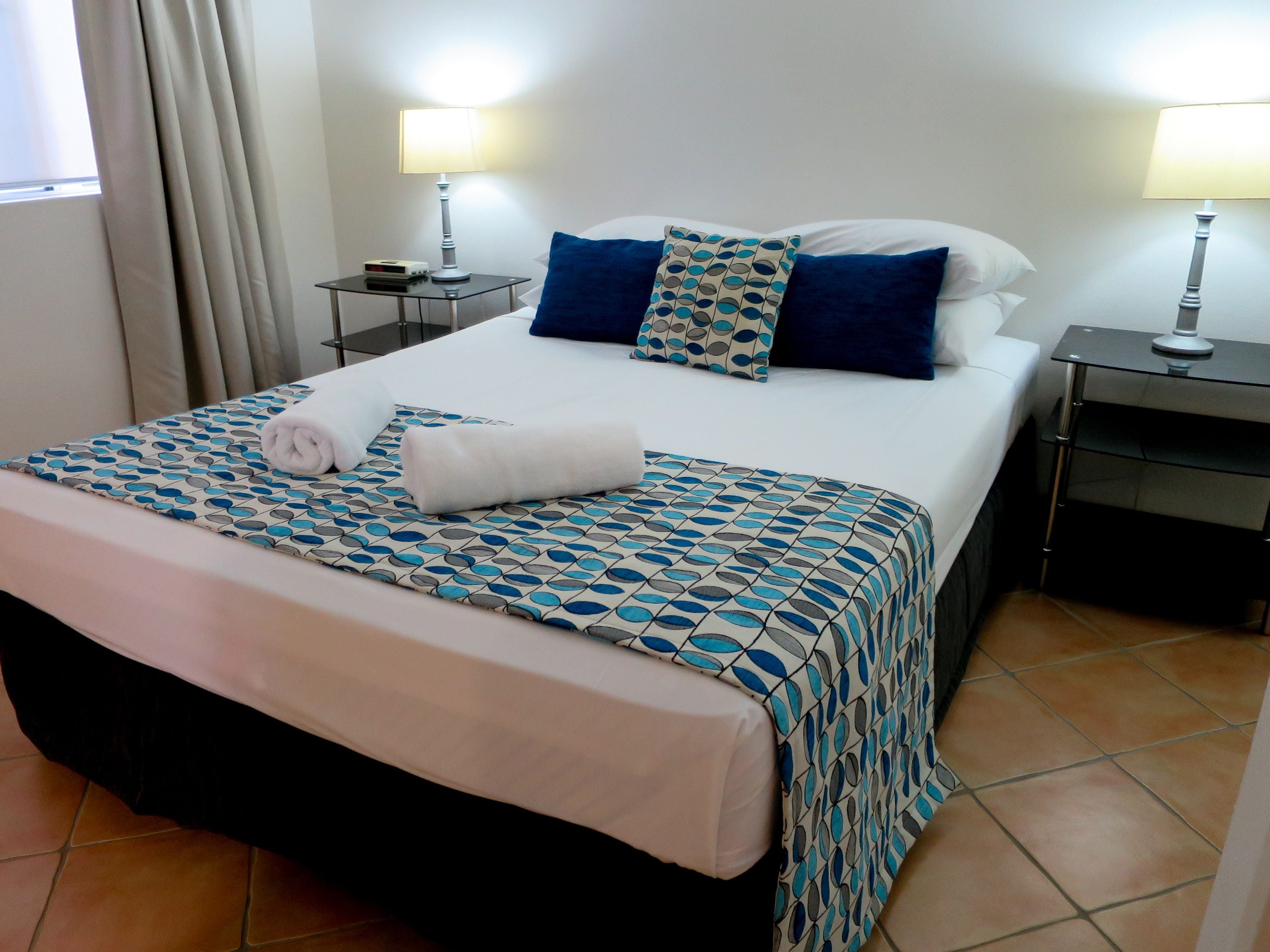 A neatly made bed with a patterned bedspread, two bedside lamps, and a small table with a clock.