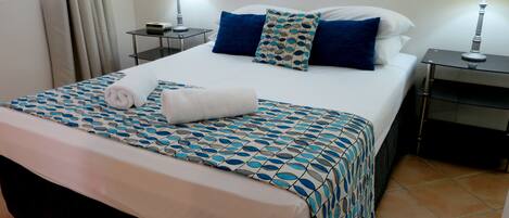 A neatly made bed with a patterned bedspread, two bedside lamps, and a small table with a clock.