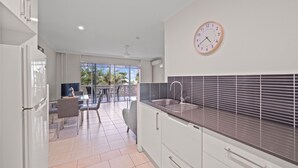 A modern kitchen with white cabinets, a dark countertop, and a wall-mounted clock. - Marlin Waters (Palm Cove)