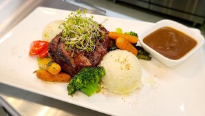 Un plato con filete, puré de papas, zanahorias, brócoli y salsa gravy.