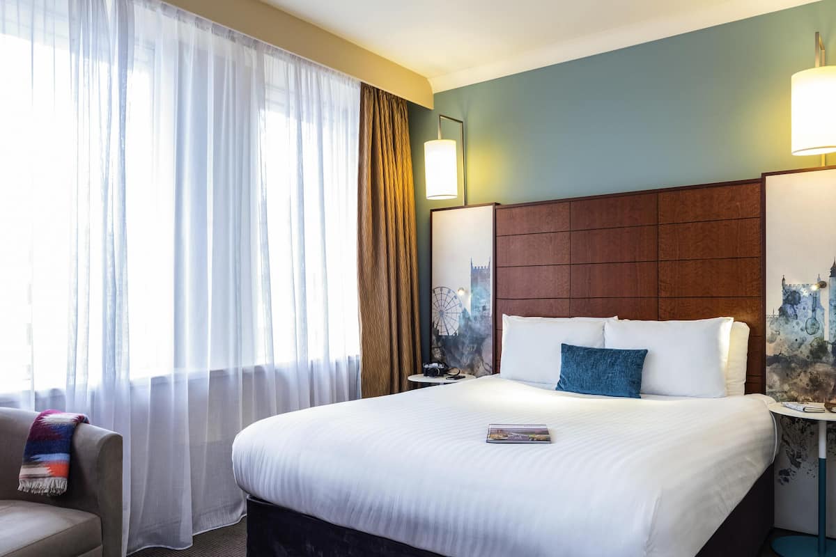Une chambre d’hôtel avec un grand lit, une table de chevet, une chaise et une vue sur le paysage urbain par la fenêtre.