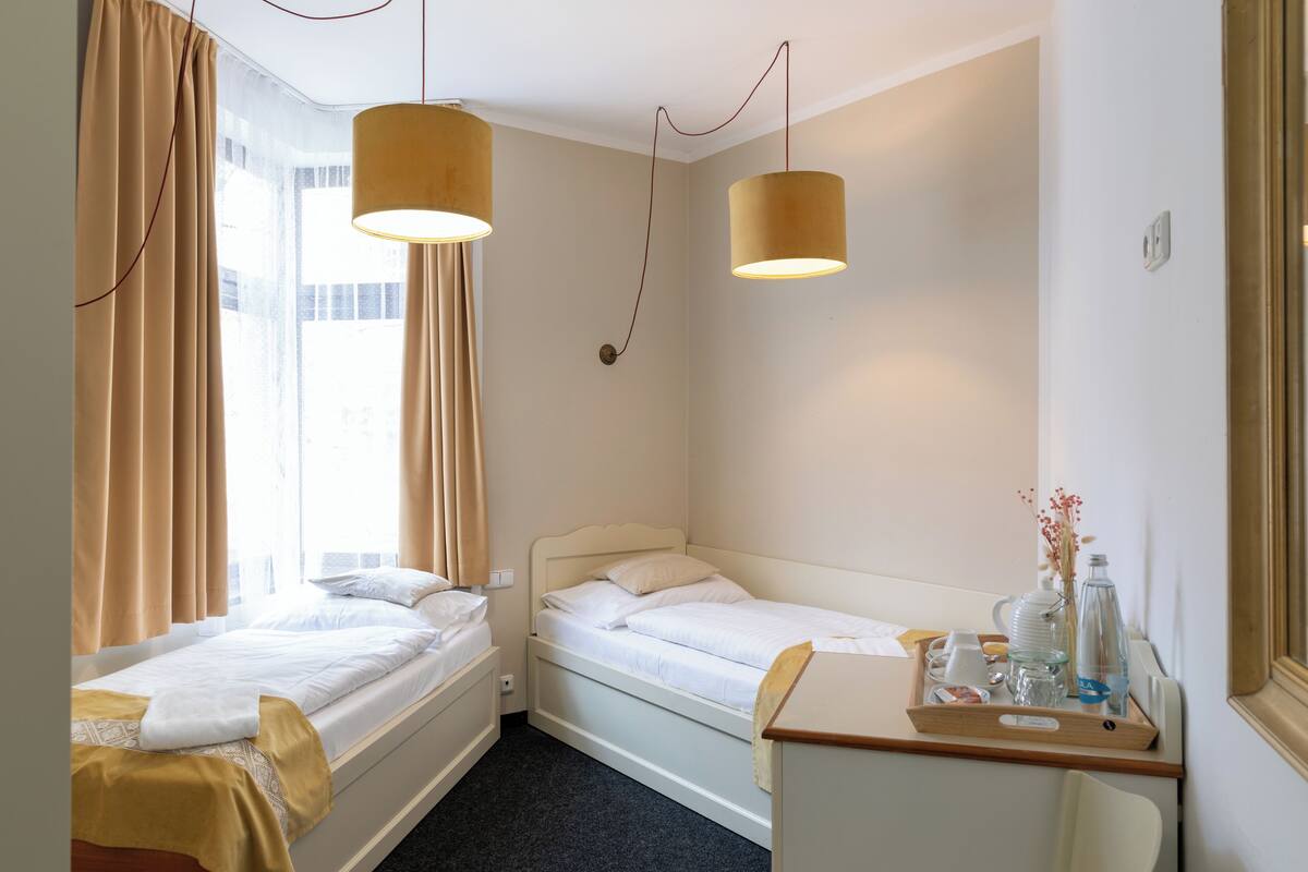 A hotel room with two single beds, a small desk with a tray of toiletries, and a window with curtains.