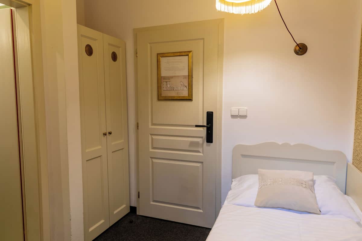A hotel room with a bed, a door with a framed notice, and a light fixture.