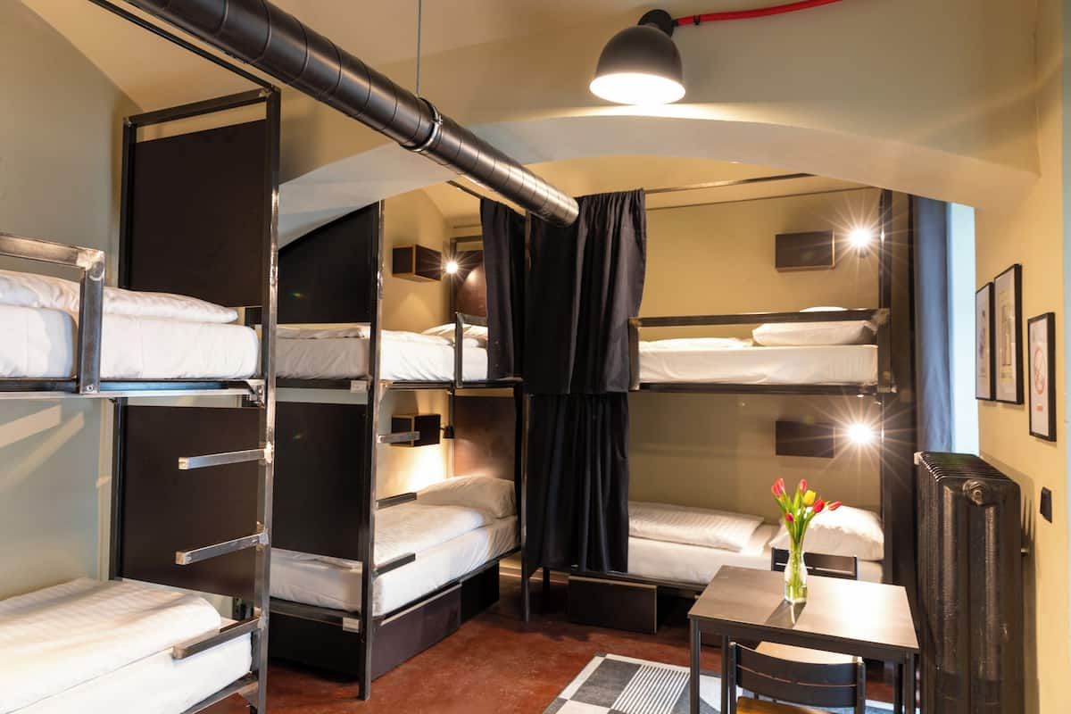 A compact hotel room with bunk beds, a small table, a chair, a desk, and a radiator.
