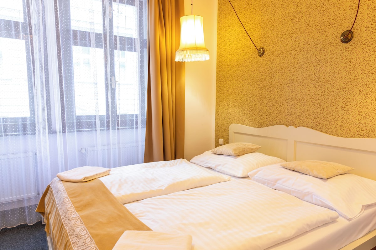 A hotel room with a large bed, a window with sheer curtains, and a patterned wall.