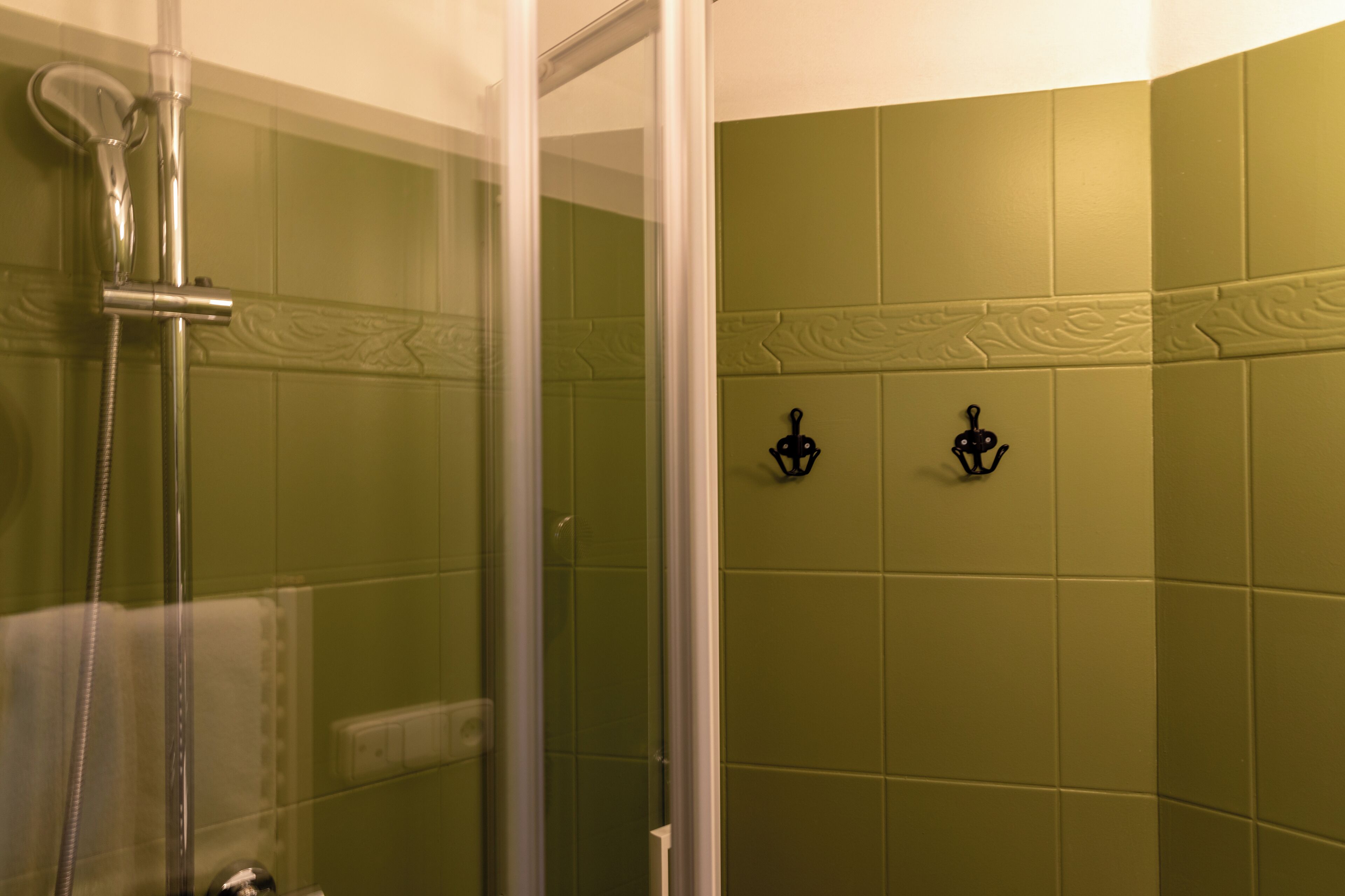 Een douchecabine met een glazen wand, een handdouche en een wandlamp.