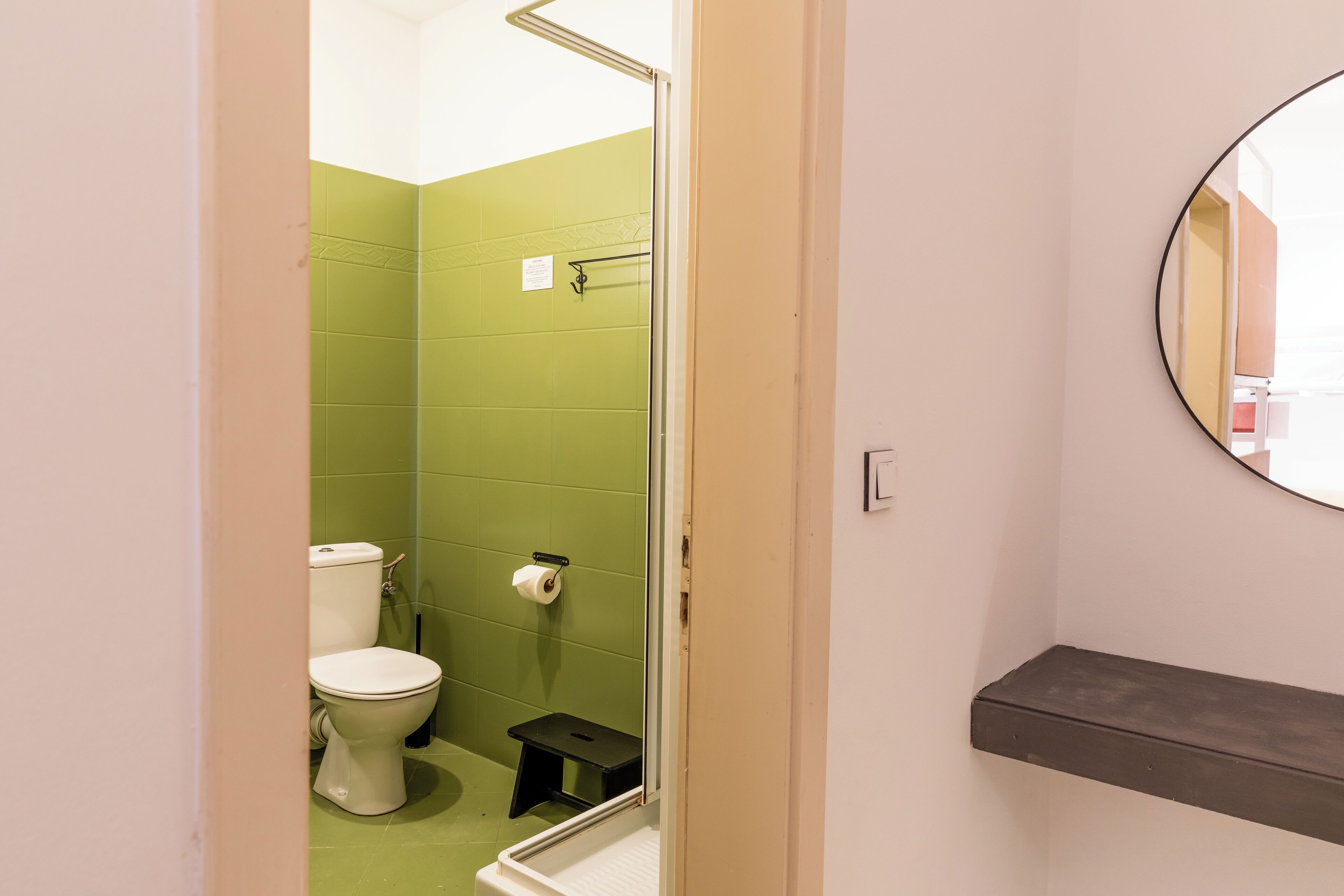 A bathroom with a toilet, a step stool, and a shelf.
