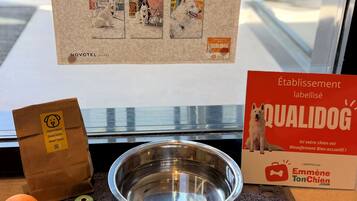 A pet-friendly hotel sign, a metal bowl, a dog food bag, a chew toy, and a dog treat.