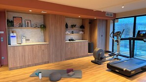 A modern gym with exercise equipment, a yoga mat, and a view of the city. - Novotel Suites Rouen Normandie (Rouen)