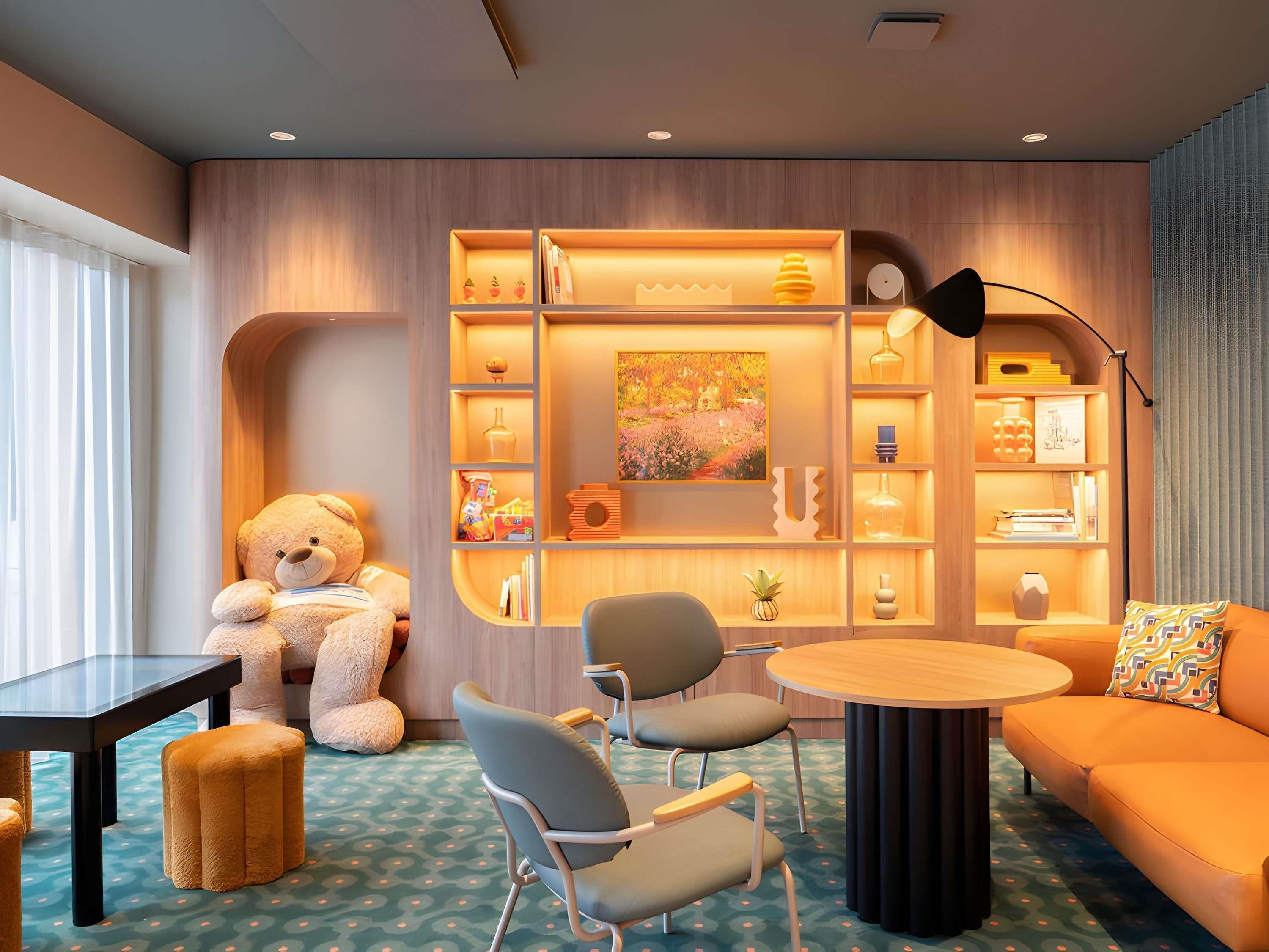 Ein gemütliches Zimmer mit einem großen Teddybär, einem runden Holztisch, zwei Stühlen, einem Sofa und einem Bücherregal mit diversen Gegenständen.