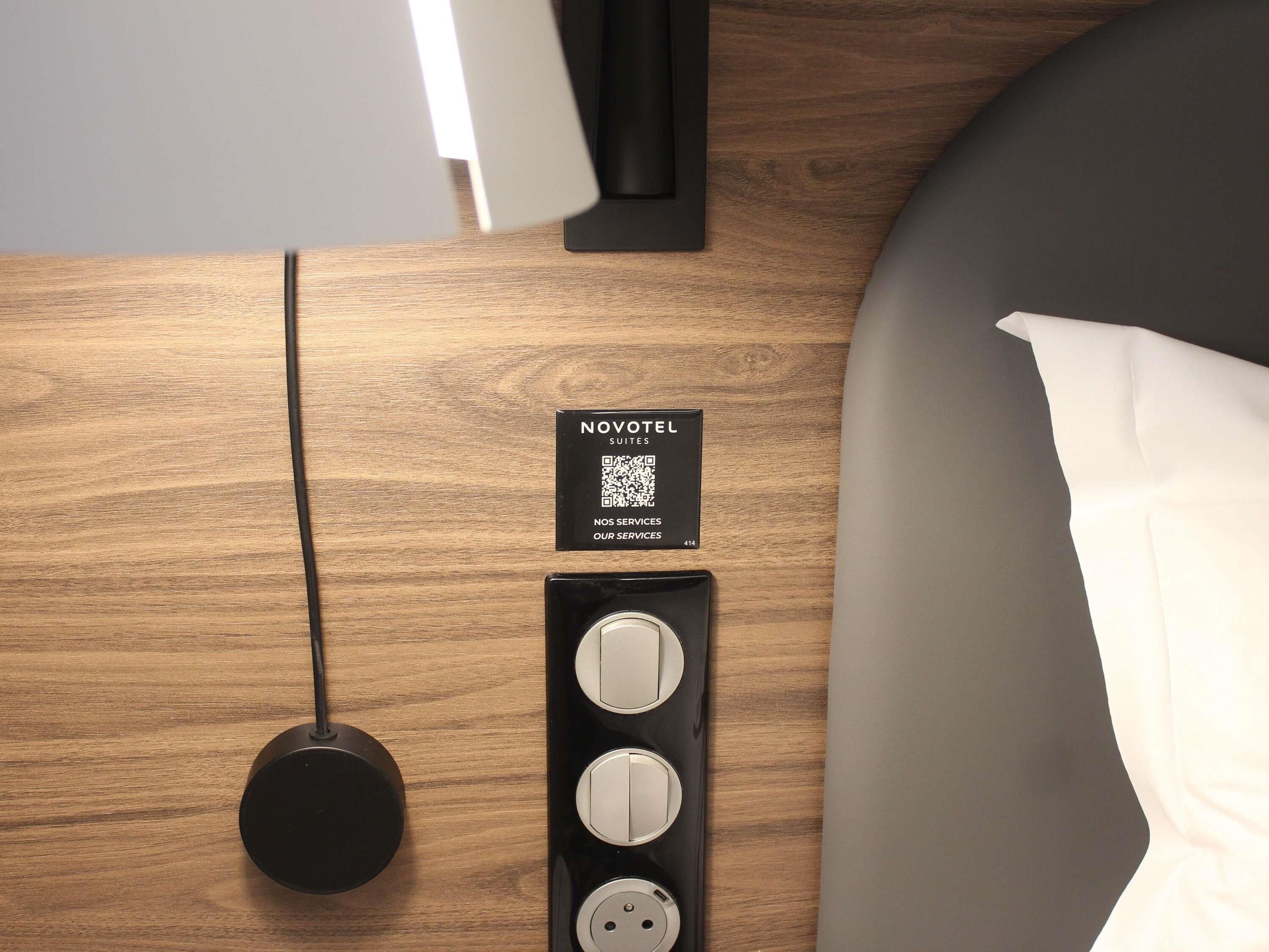 Puisesta työpöydästä löytyy Novotel Suites -kyltti, QR-koodi sekä musta latausasema, jossa on kolme liitäntäpistoketta.