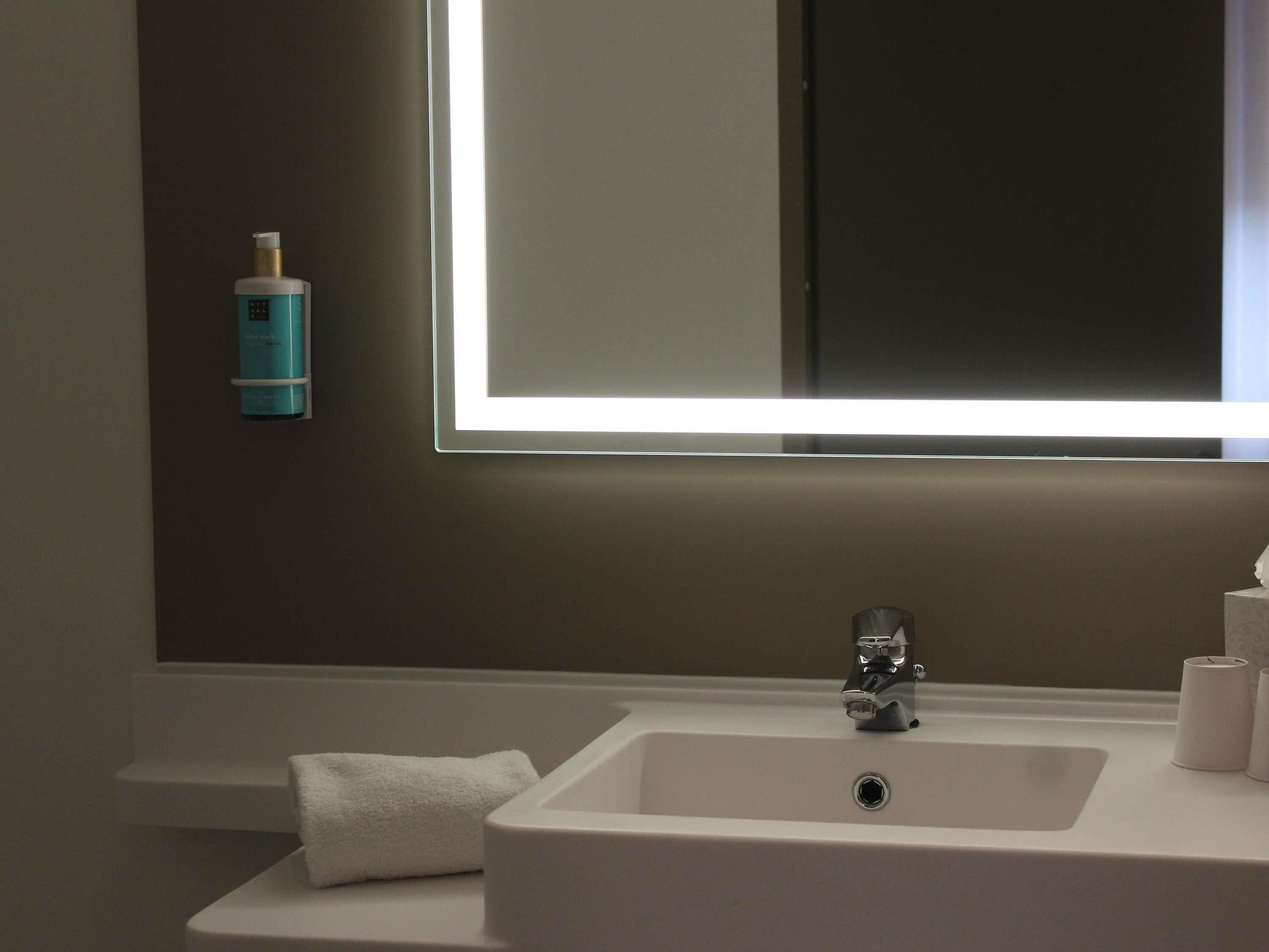 Een badkamer met een witte wastafel, een spiegel en een handdoek.