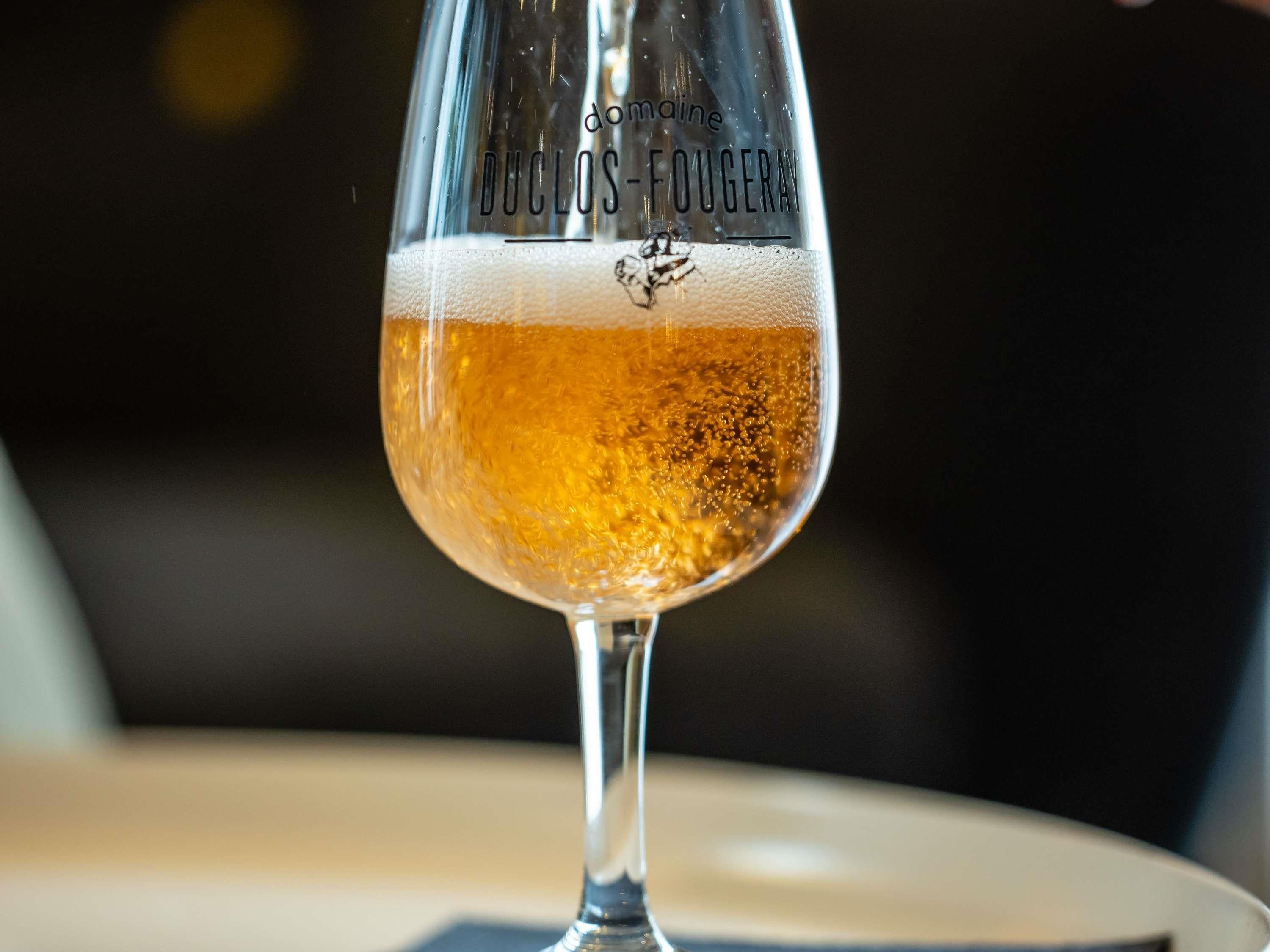 A glass of Duclos-Fougeray wine with a frothy head, placed on a table.