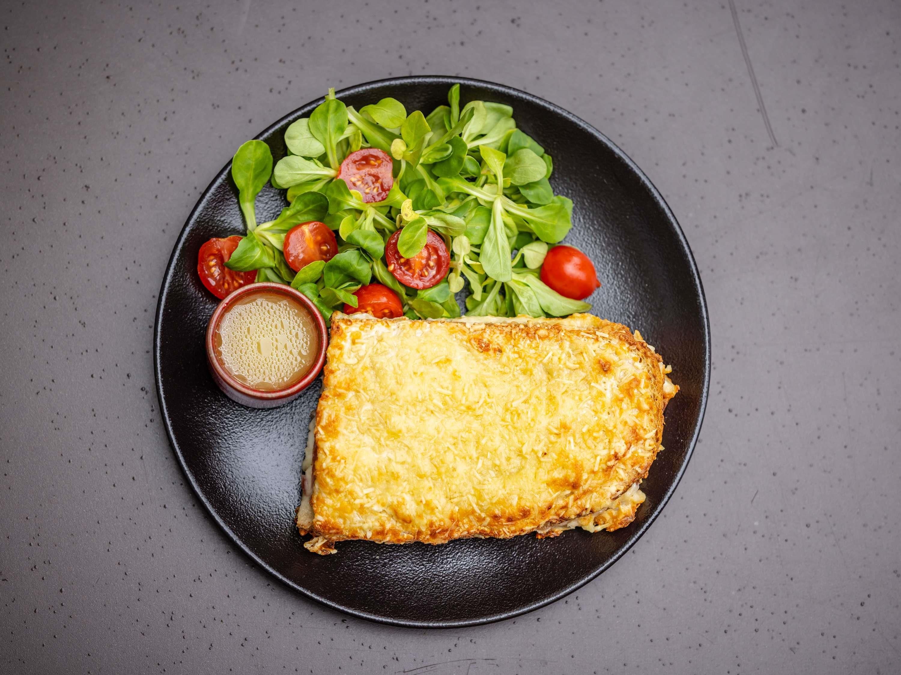 Um prato com um sanduíche de queijo grelhado, uma salada com tomates cereja e uma pequena tigela de mostarda.