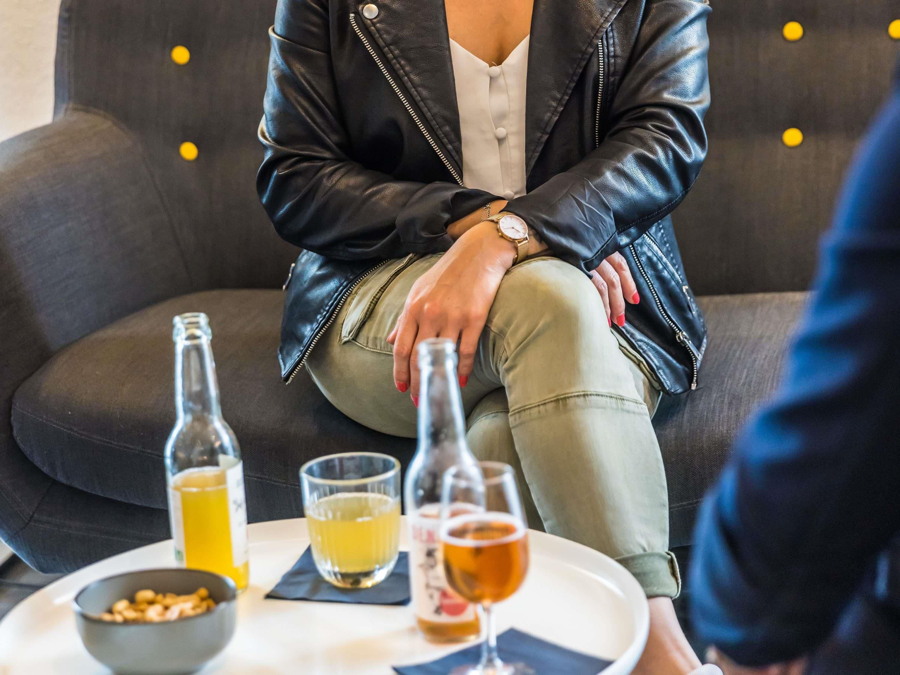Une personne est assise sur un canapé, devant lequel se trouve une table avec des bouteilles et des verres.