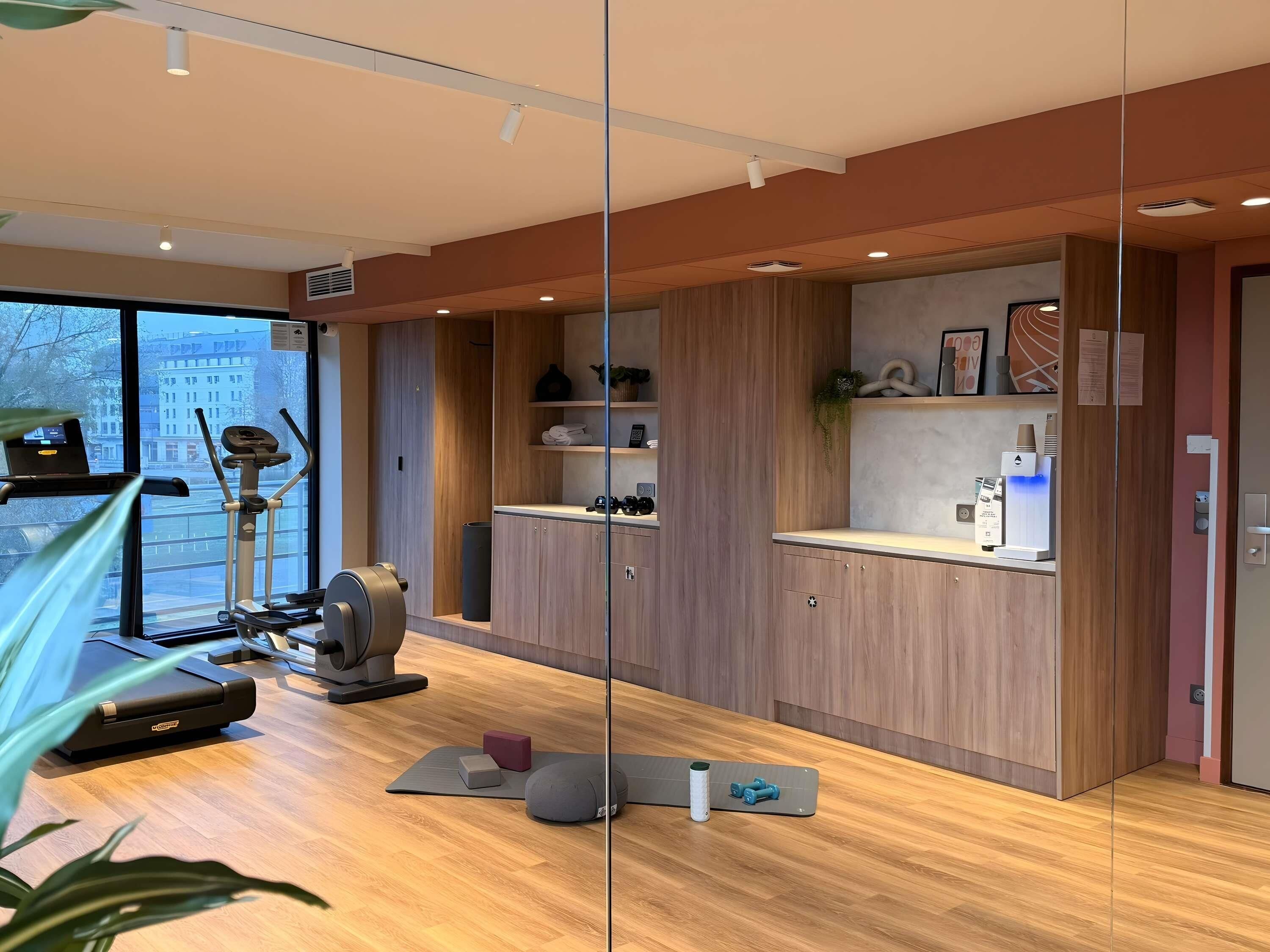 A modern gym with exercise equipment, wooden cabinets, and a large window.