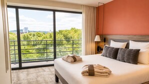 Een hotelkamer met een groot raam, een bed met kussens, een bedlampje en een telefoon.