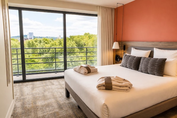 A hotel room with a large window, a bed with pillows, a bedside lamp, and a telephone.
