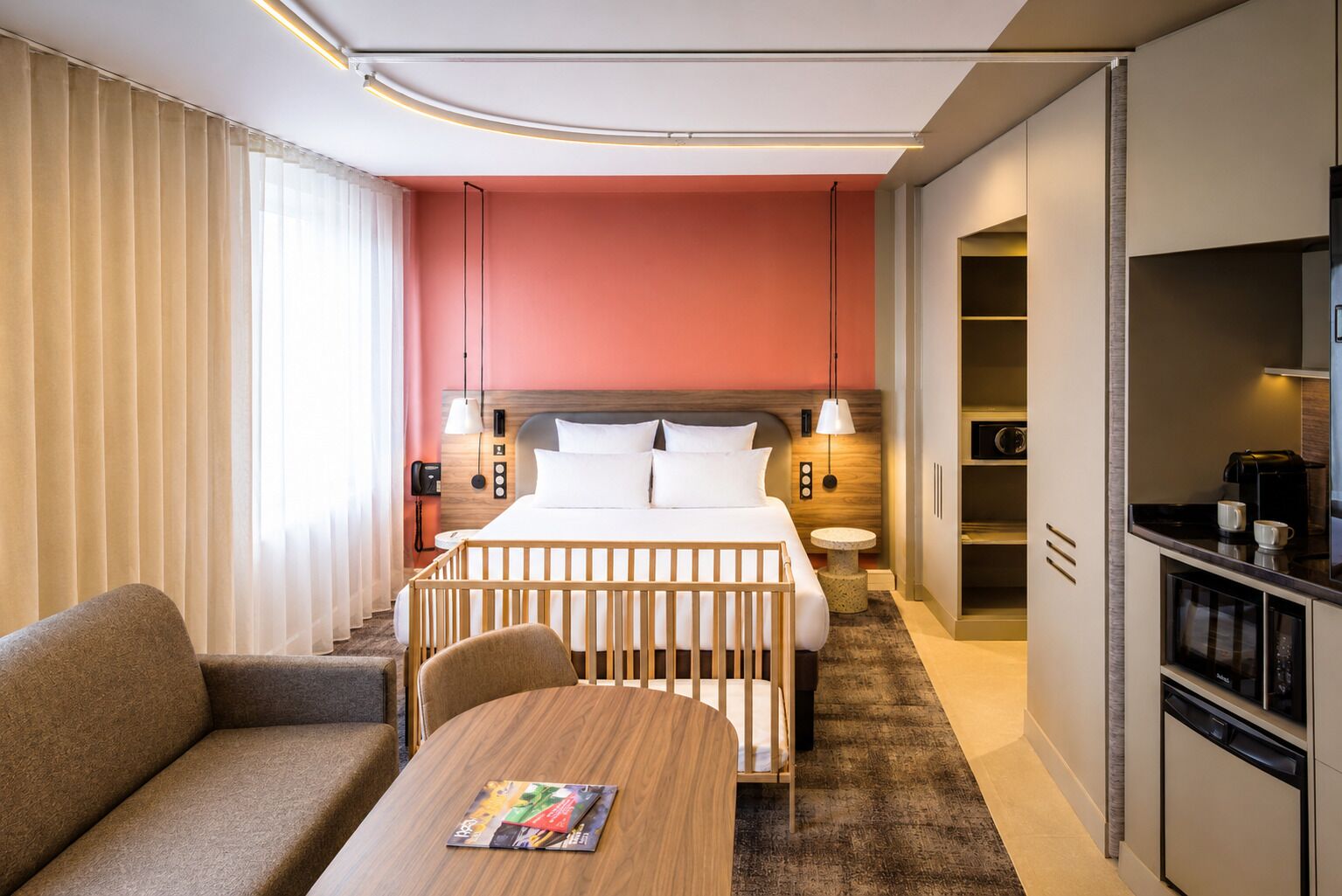 A hotel room with a bed, bedside tables, a desk, a chair, a sofa, a dining table, and a kitchenette.