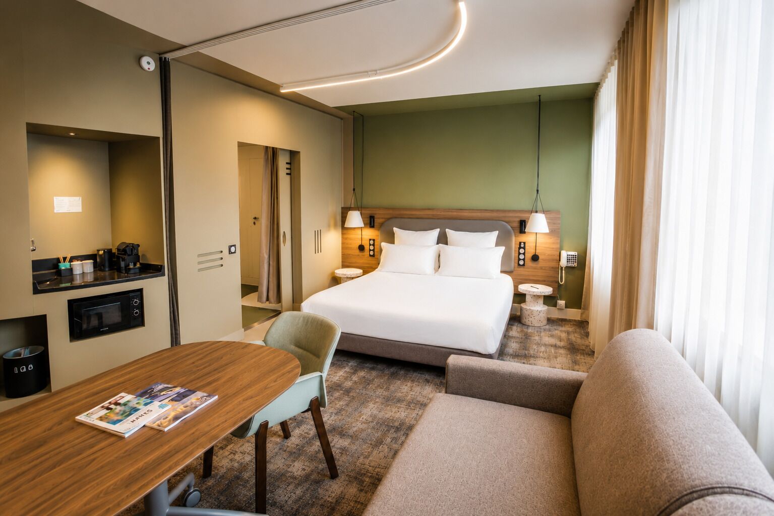 Habitación de hotel con cama, escritorio, silla, sofá, mesita, lámpara y teléfono.