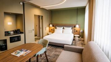 Habitación de hotel con cama, escritorio, silla, sofá, mesita, lámpara y teléfono.