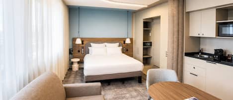 Una habitación de hotel con cama, sofá, mesa, kitchenette y baño.
