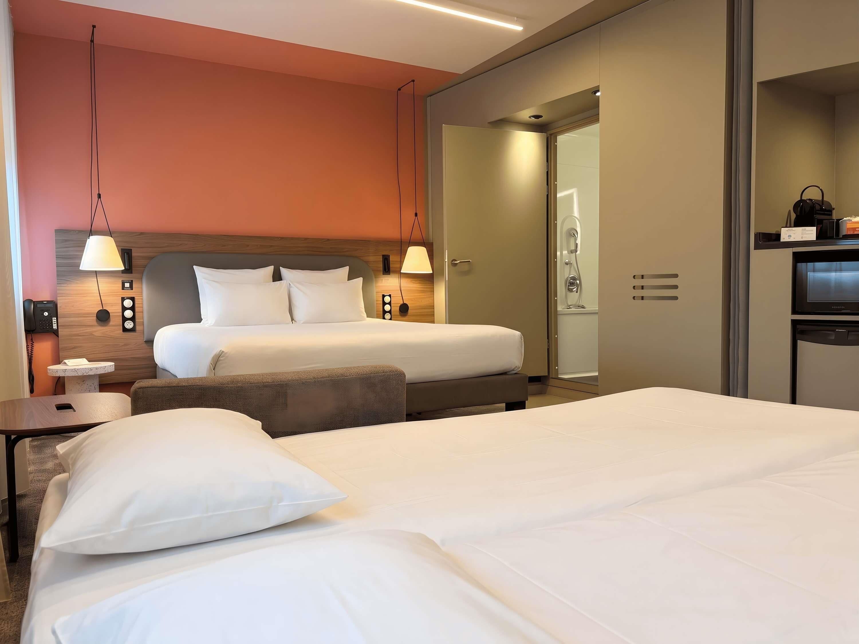 A hotel room with two beds, a desk, a chair, a wardrobe, and a shower area.