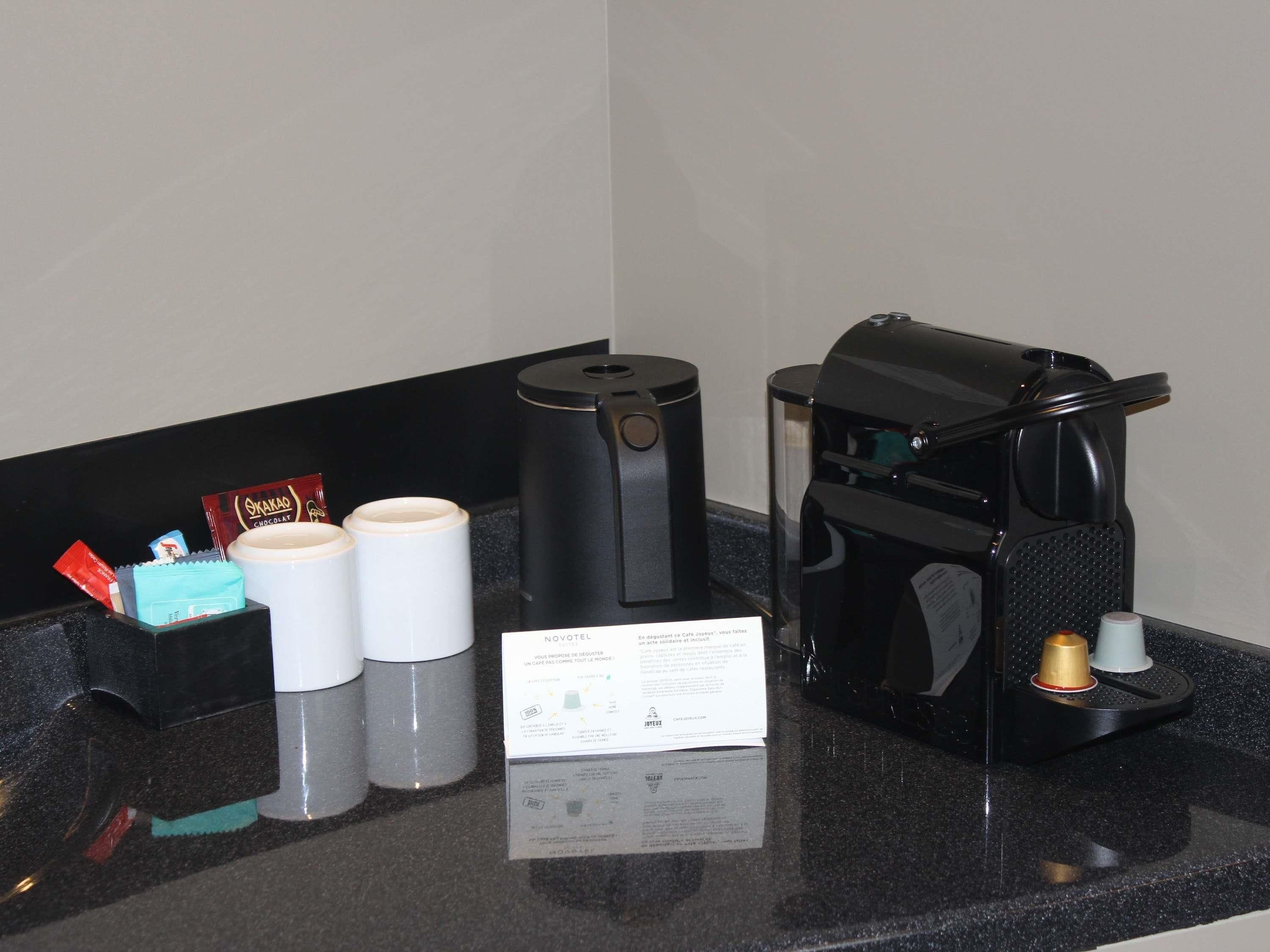 A coffee machine, two white cups, and a packet of chocolate on a countertop.