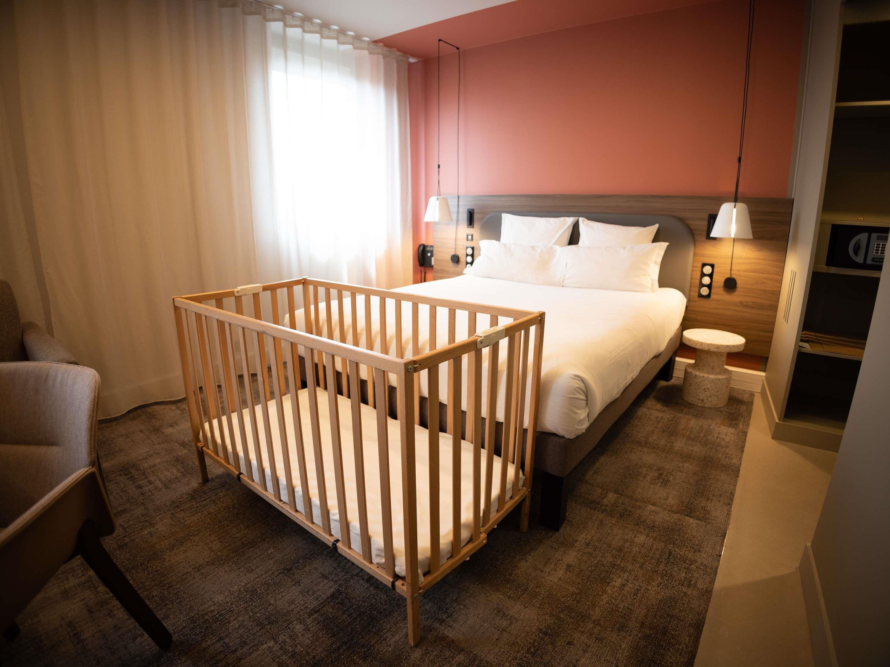 Une chambre d’hôtel équipée d’un berceau, d’un lit, d’une table de chevet, d’une lampe et d’une petite table.