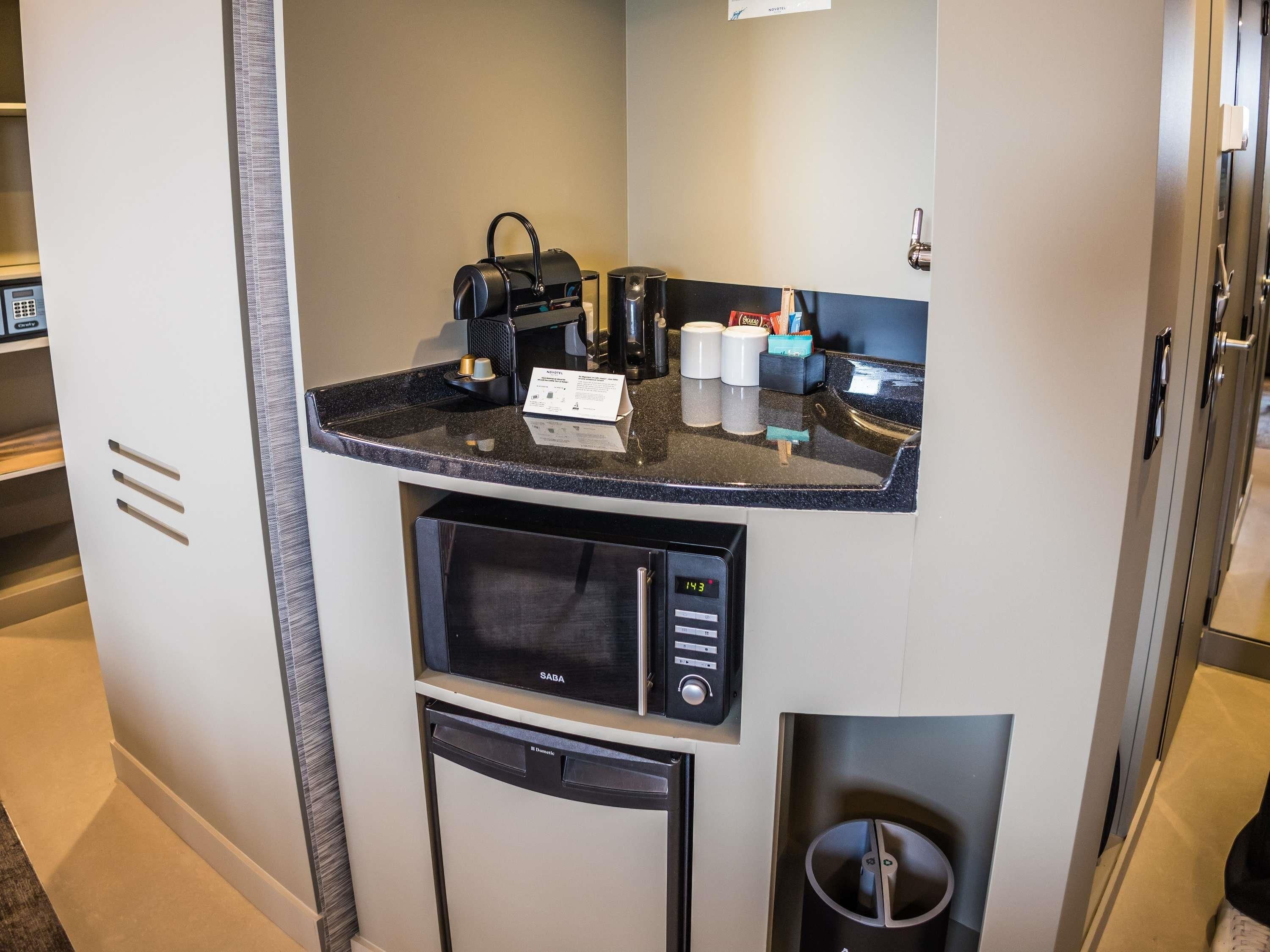 Una kitchenette compacta equipada con microondas, cafetera y un pequeño bote de basura.
