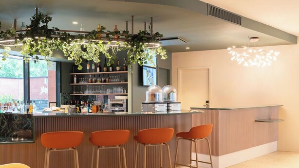 Un  área de bar moderna con una barra, taburetes y un espacio de estar con una mesa redonda.