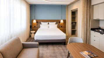 A hotel room with a bed, a sofa, a dining table, a small round table, and a kitchenette.