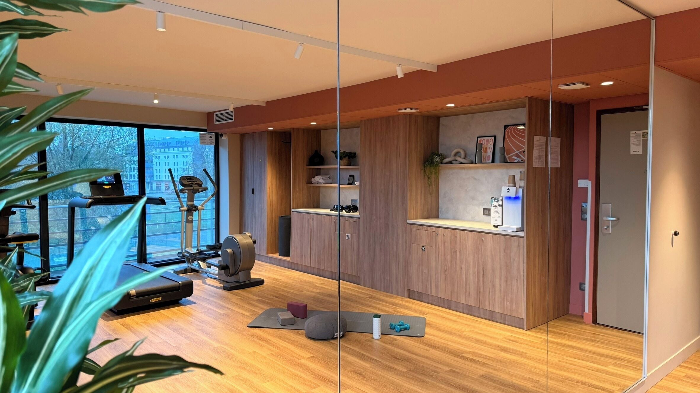 A modern gym with exercise equipment, wooden cabinets, and a large window.