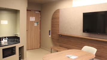 Habitación de hotel con kitchenette, televisor de pantalla plana montado en la pared, una mesa de madera y una sola silla.