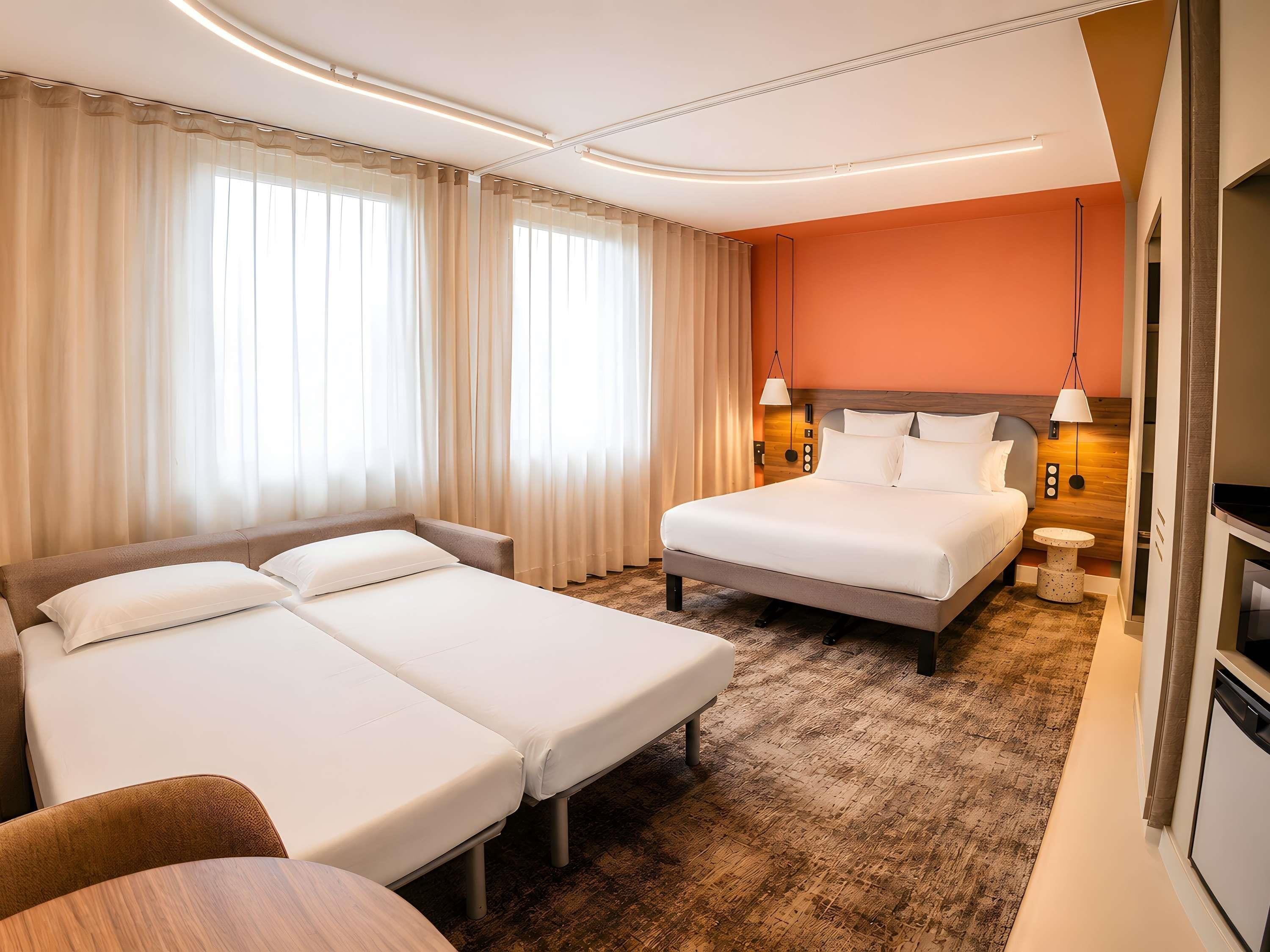 Habitación de hotel con dos camas, un sofá, una mesita y un televisor.