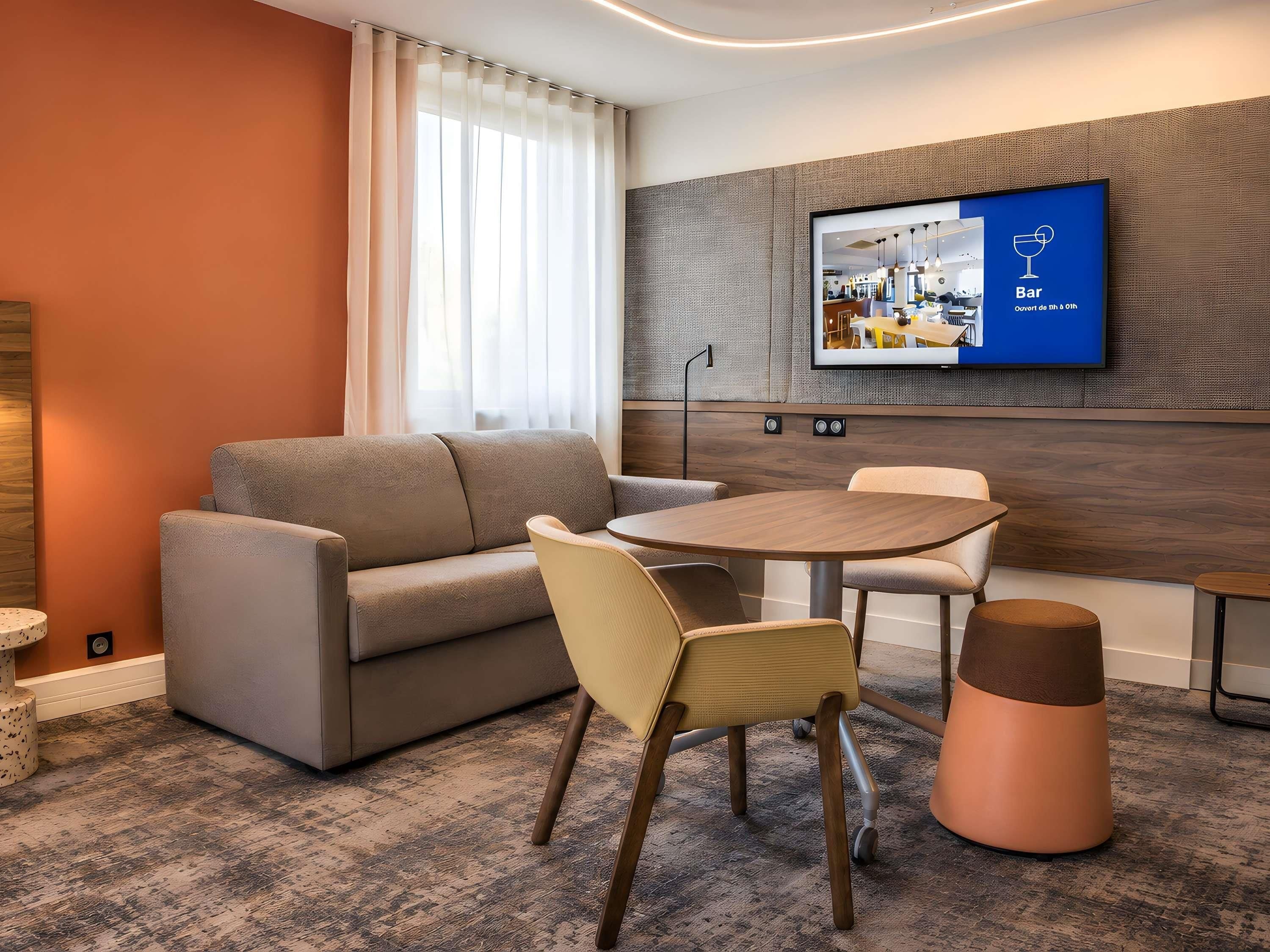 Une chambre d’hôtel moderne équipée d’un canapé, de fauteuils, d’une table ronde et d’un téléviseur fixé au mur.