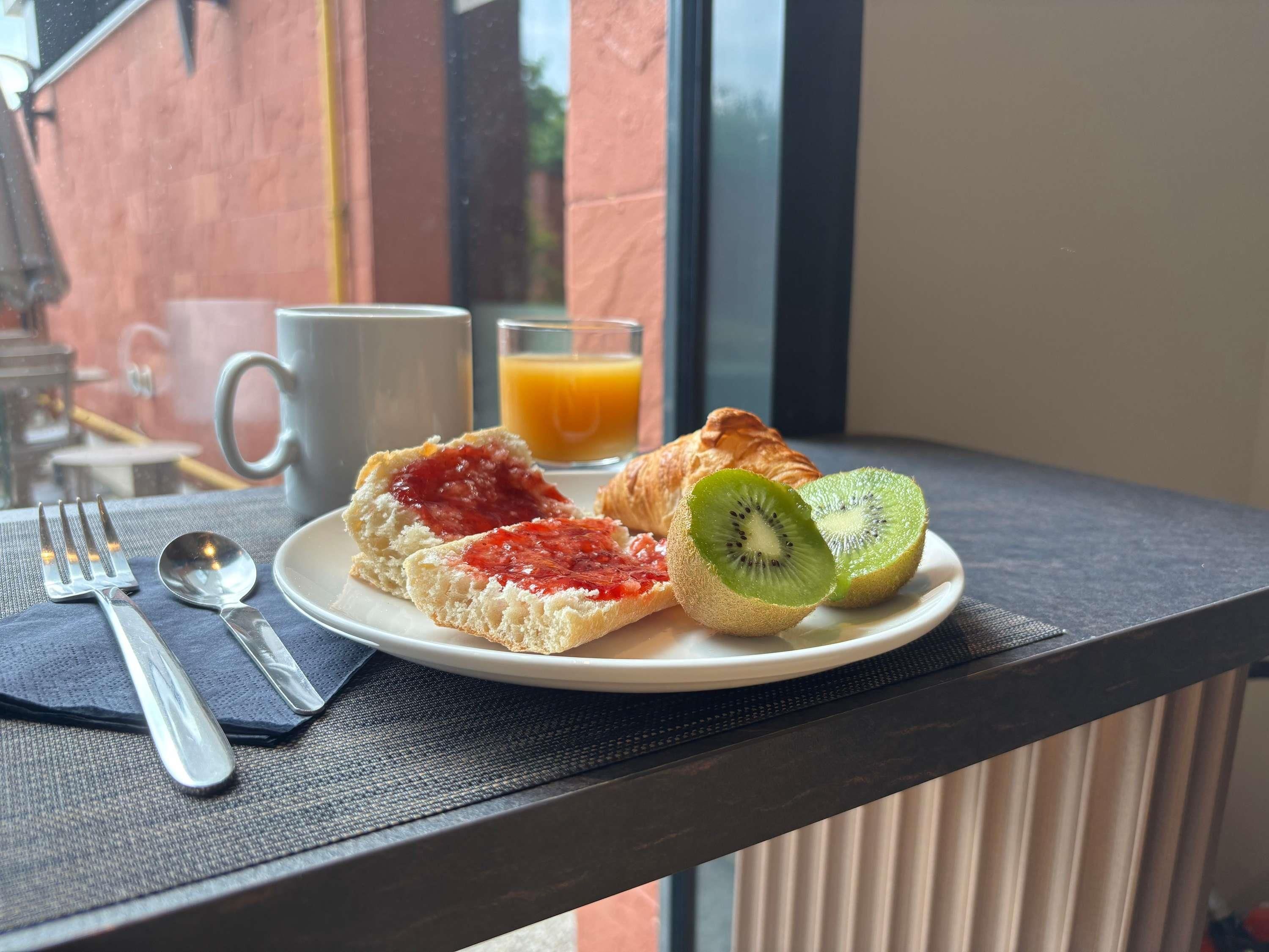 Ein Frühstücksteller mit Toast, Marmelade und Kiwi auf einem Tisch mit Blick aus dem Fenster.