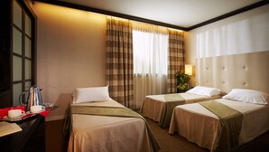 Une chambre d’hôtel avec deux lits, un bureau avec une machine à café et une fenêtre avec des rideaux.