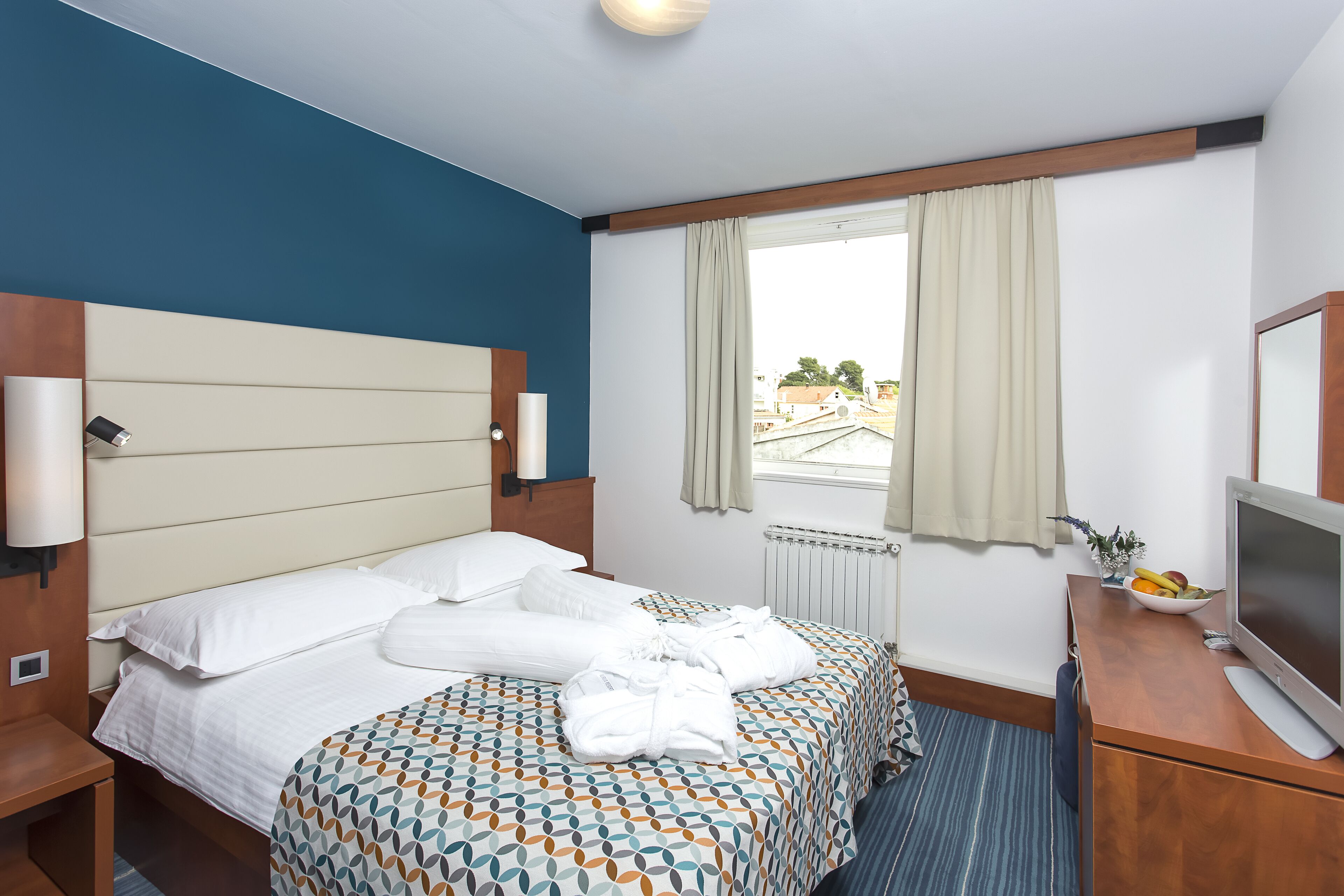 Een hotelkamer met een bed, een bureau met een televisie en een raam met gordijnen.